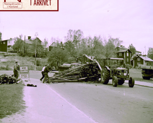 På bilden syns en traktor vars släp fyllt med någon form av klenare träd eller stolpar. Platsen som detta skett är i Härnösand vid viadukten och året är 1959. Bilden kommer från Norrfotos arkiv.